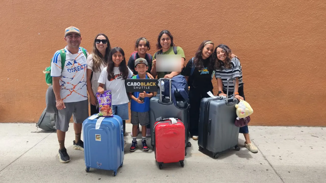 Family of eight with luggage holding a Cabo Black Shuttle sign after arriving at SJD airport