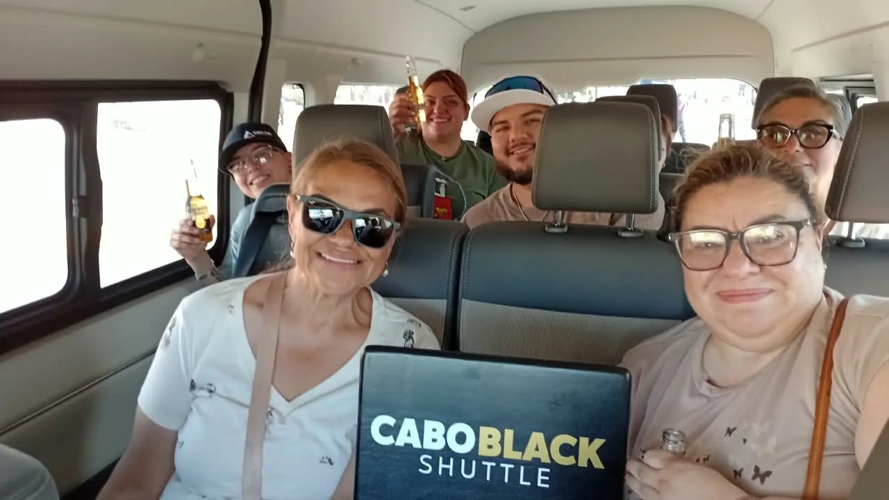 Six passengers in a private Cabo group shuttle van holding a Cabo Black Shuttle sign