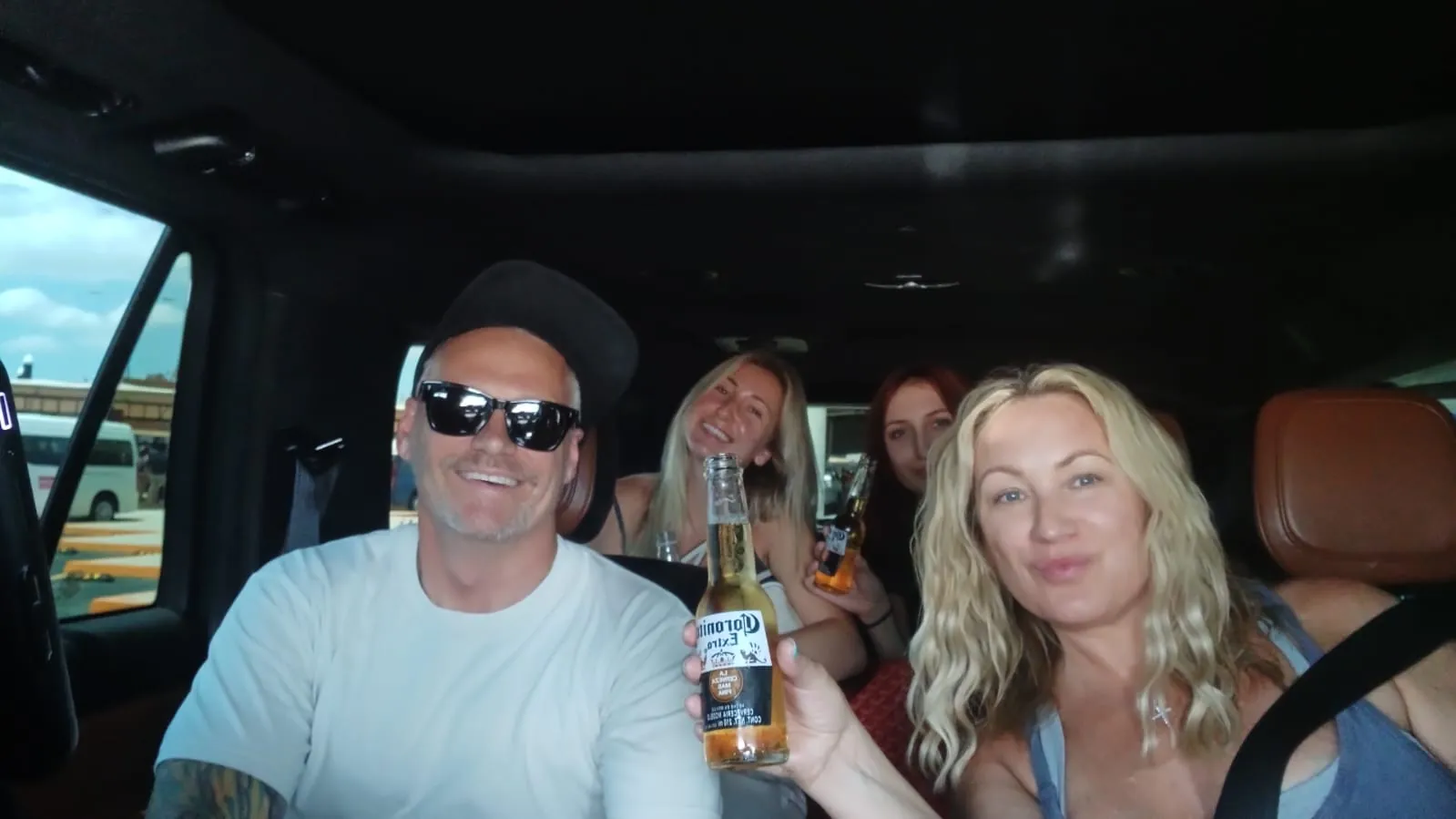 Four passengers holding cold beers in the back of a private Cabo shuttle SUV