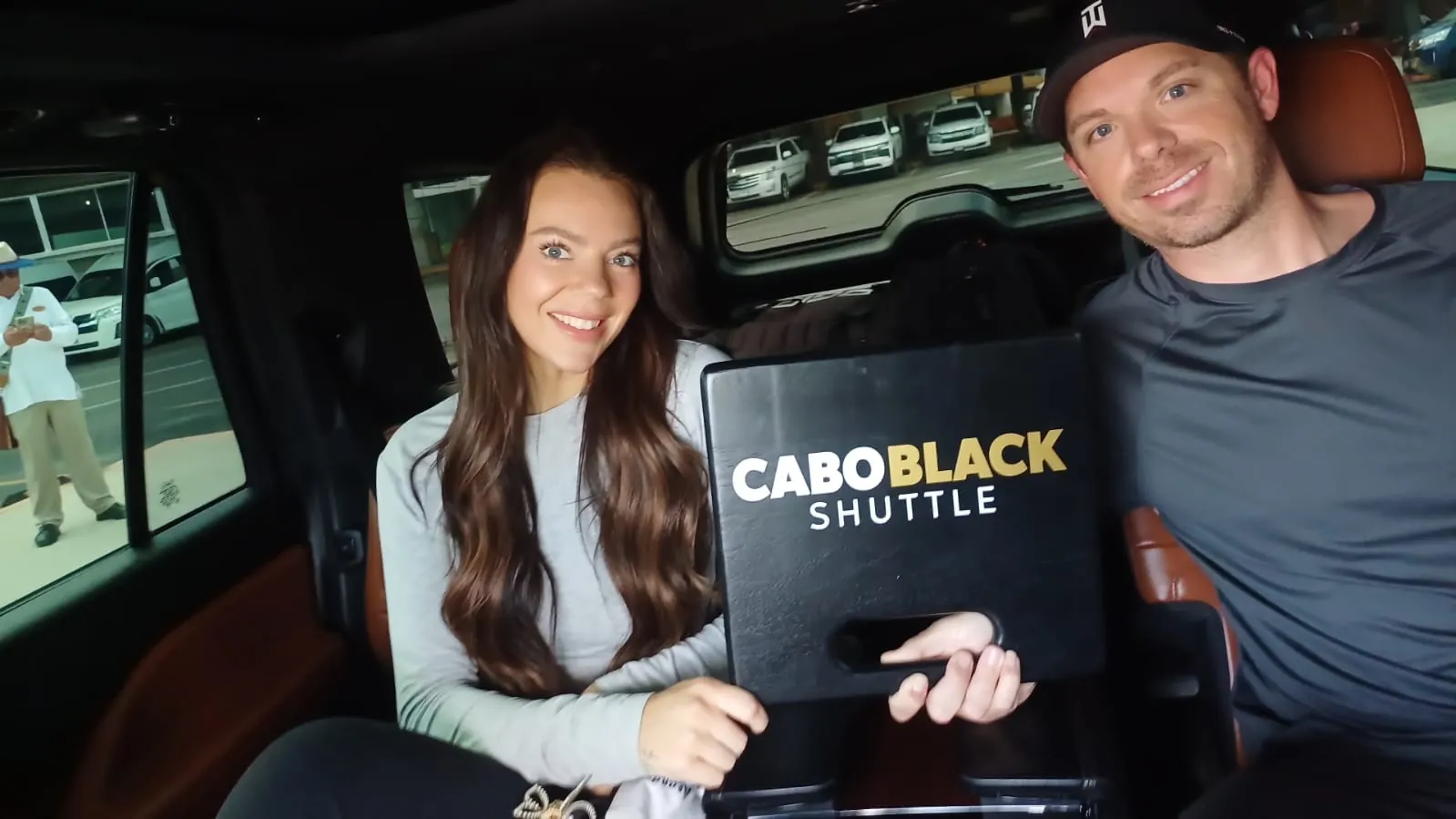 Couple holding a Cabo Black Shuttle sign in the back seat of a private airport shuttle SUV at SJD